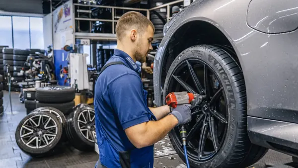 Mechaniker schraubt ein Rad mit dem Schlagschrauber an ein graues Auto