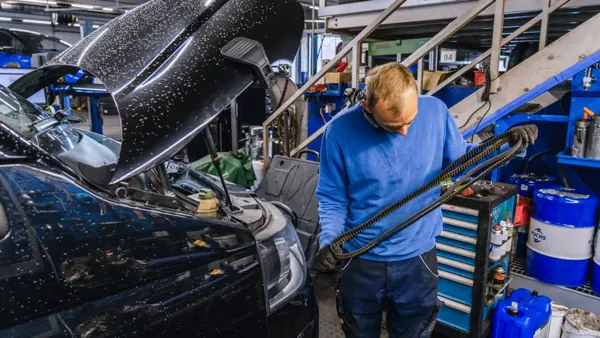 Mechaniker hält einen Keilrippenriemen vor einer offenen Motorhaube
